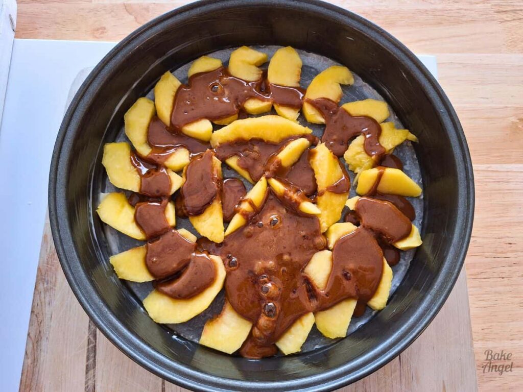 Caramel sauce poured over peach slices in a cake pan.