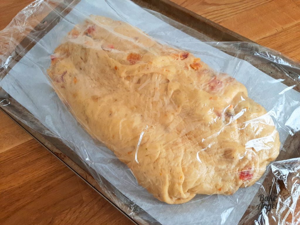 Raw stollen dough covered in plastic wrap while it proves.