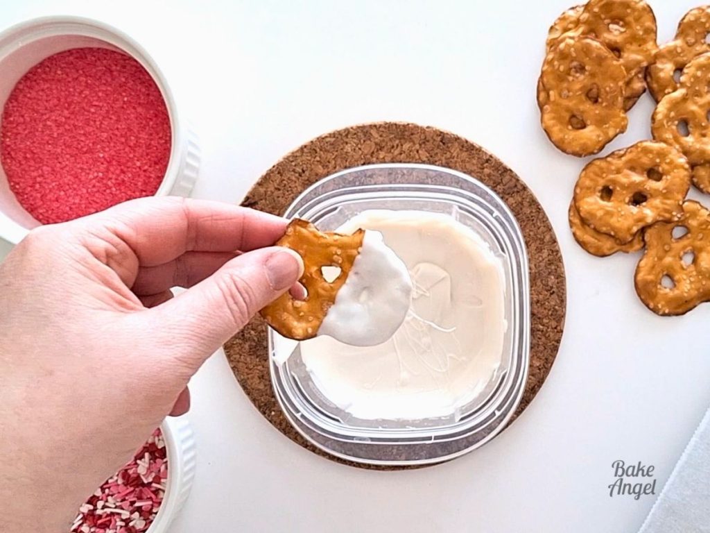 Dipping a pretzel in melted white chocolate.
