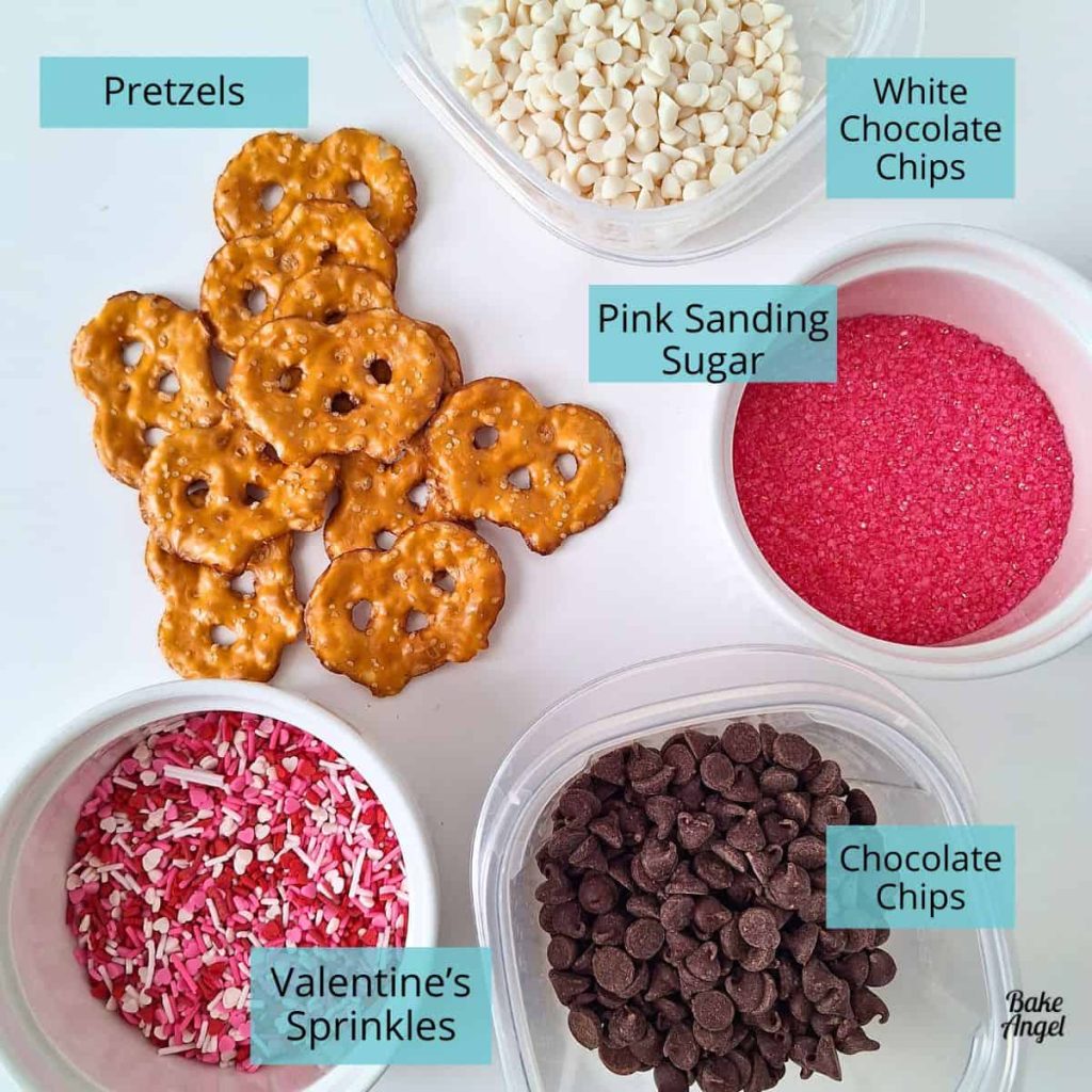 Pretzels, White Chcolate Chips, Chocolate Chips, Pink Sanding Sugar and Valentine's Sprinkles on a white countertop.