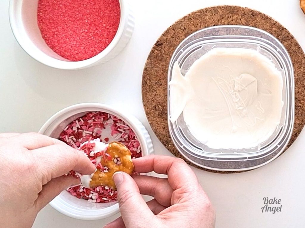 Adding Valentine's Day sprinkles to a white chocolate dipped pretzel.