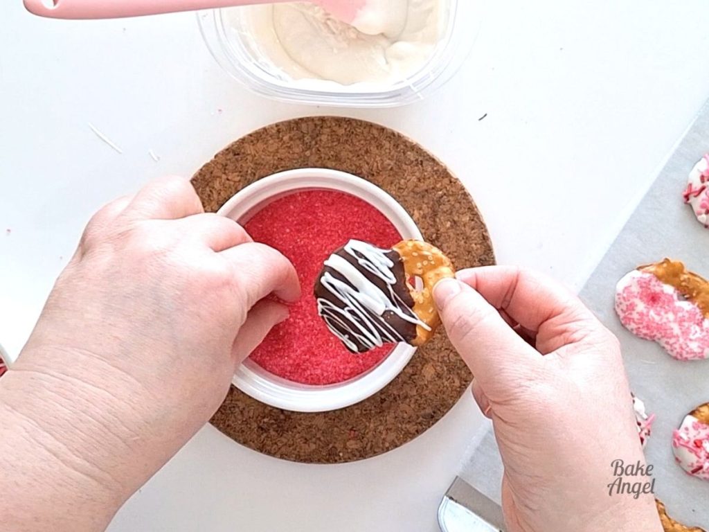 Adding pink sanding sugar to a chocolate dipped pretzel.