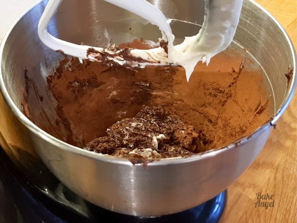 A stand mixer bowl with shortening, butter, cocoa powder and vanilla being mixed.