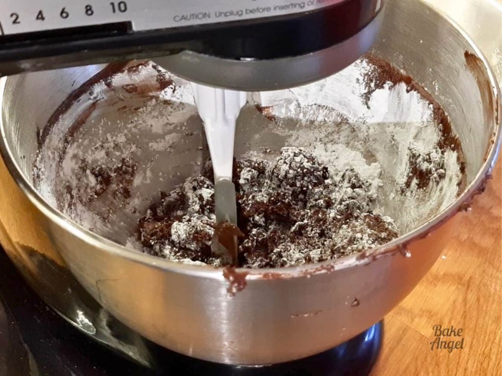 Icing sugar being stirred in to buttercream mixture in a stand mixer bowl.