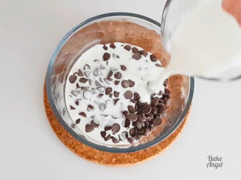 Hot coconut cream being poured over a small bowl of chocolate chips.