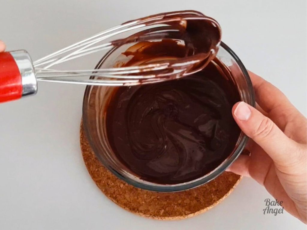 A whisk being held above a small bowl of Dairy Free Chocolate Ganache.