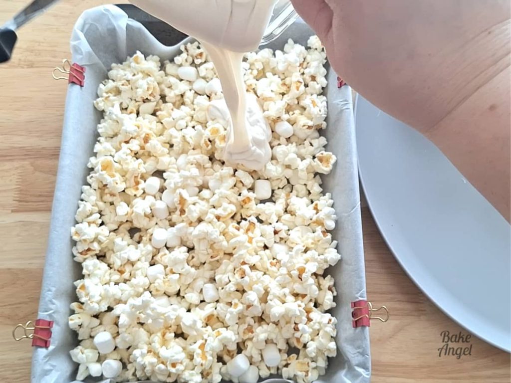 Melted white chocolate being added to popcorn for Easter bunny bait recipe.