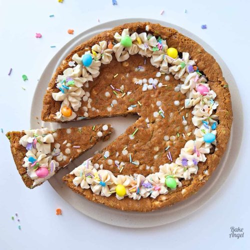 A Vegan Easter Cookie Cake on a plate with one slice cut and slightly removed on the left side.