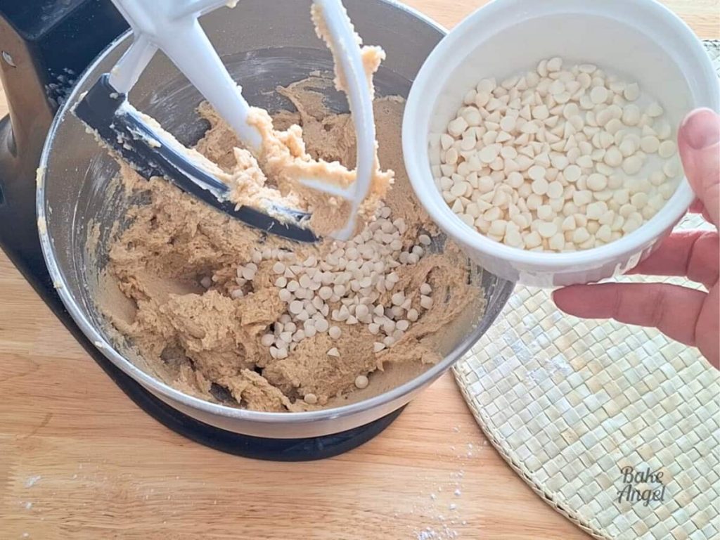 Adding chocolate chips to cookie dough in a mixing bowl.