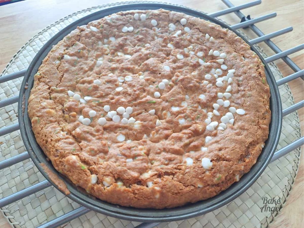 Freshly baked vegan easter cookie cake in the baking pan on a cooling rack. The top of the cake is lightly golden.