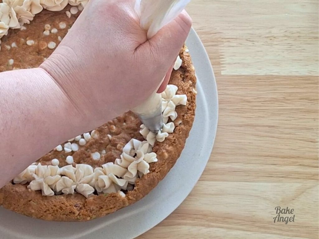 Piping buttercream icing stars on the outside edge of a baked cookie cake.