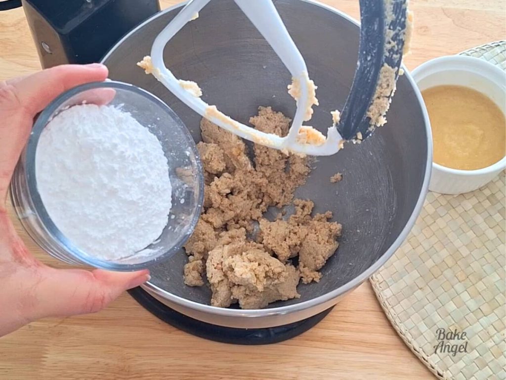 Adding icing sugar into a mixing bowl containing mixed butter and brown sugar.