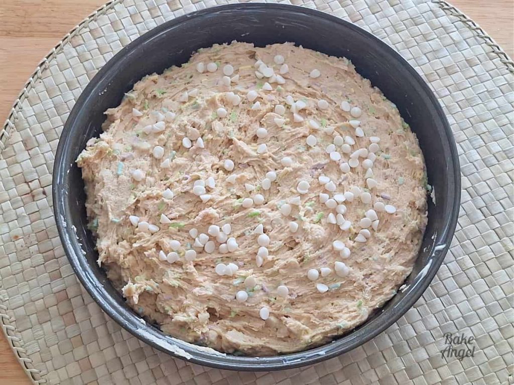 Raw cookie dough with white chocolate chips on top, in a round 9 inch pan before baking.