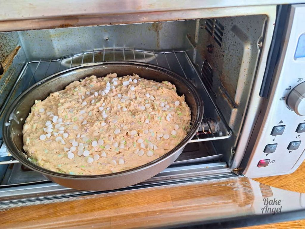 A 9 inch vegan easter cookie cake being placed into a toaster oven to bake.