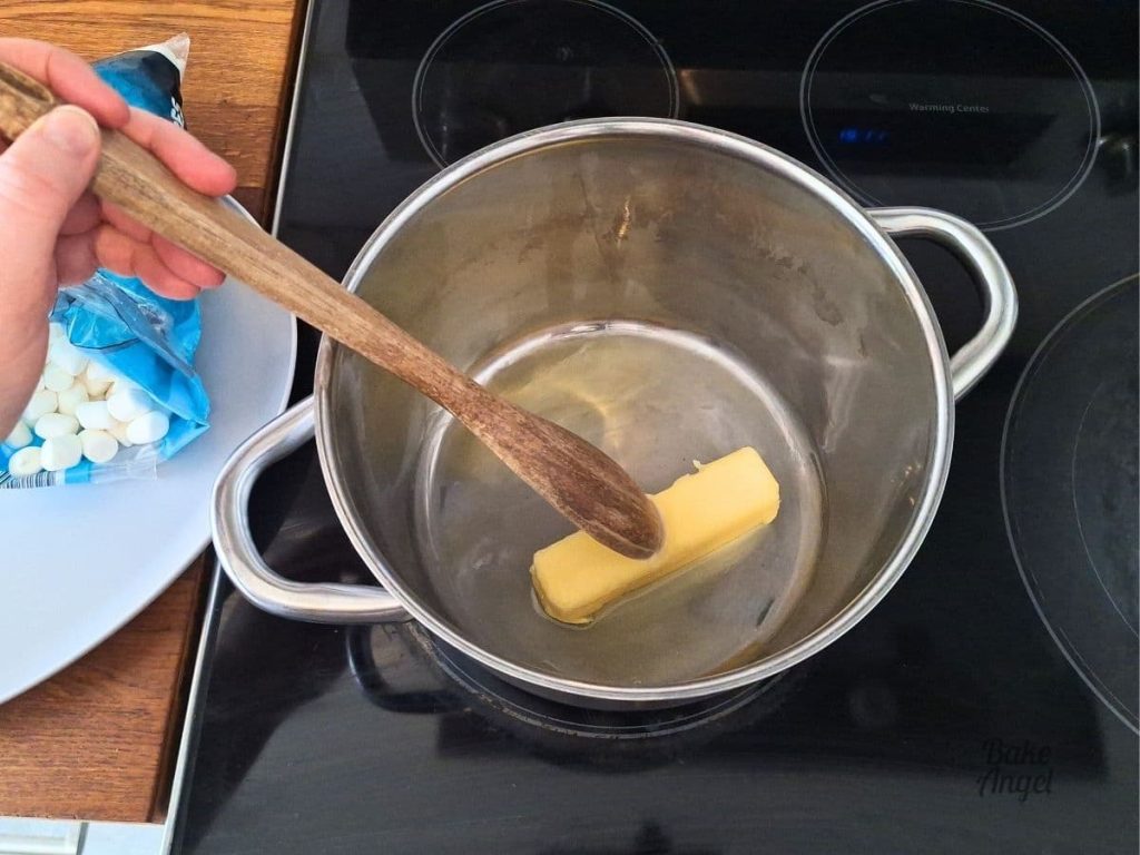 A stick of butter being stirred in a saucepan over a medium heat to melt it.