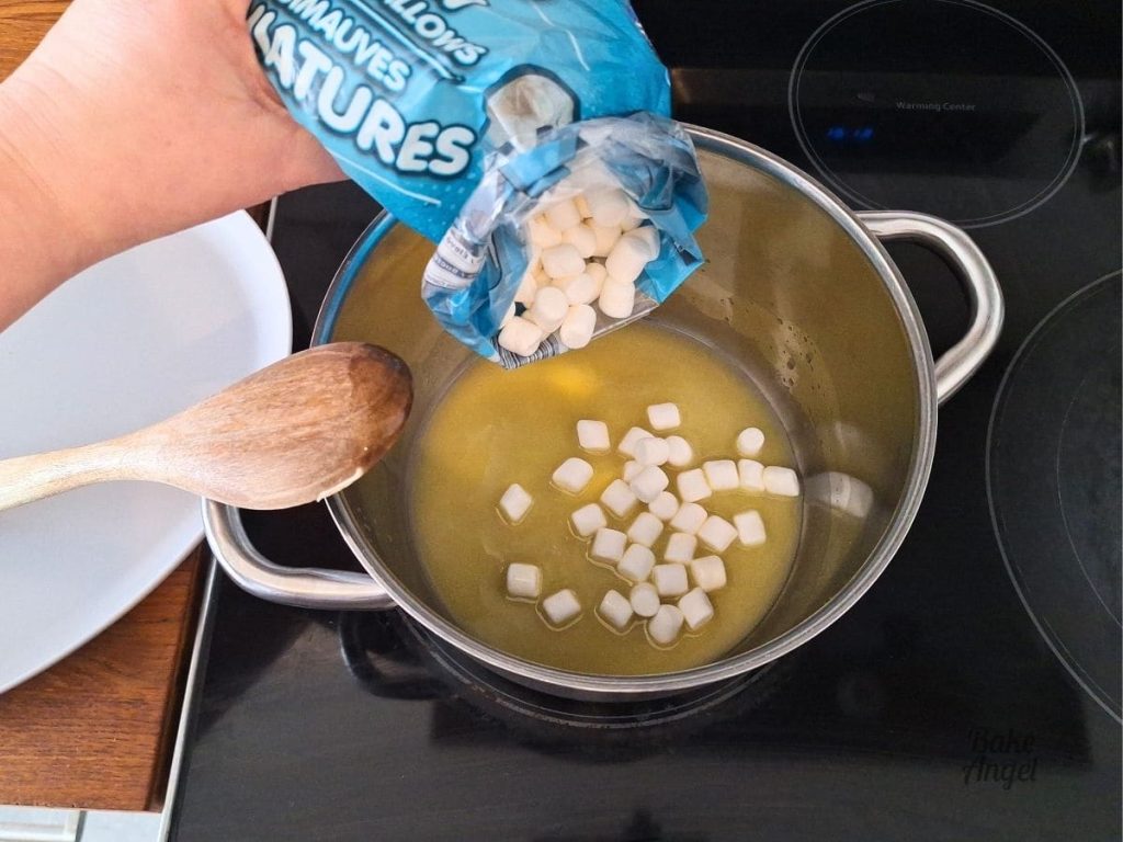 Mini marshmallows being added to a large saucepan with melted butter to make Rice Krispie Treats.