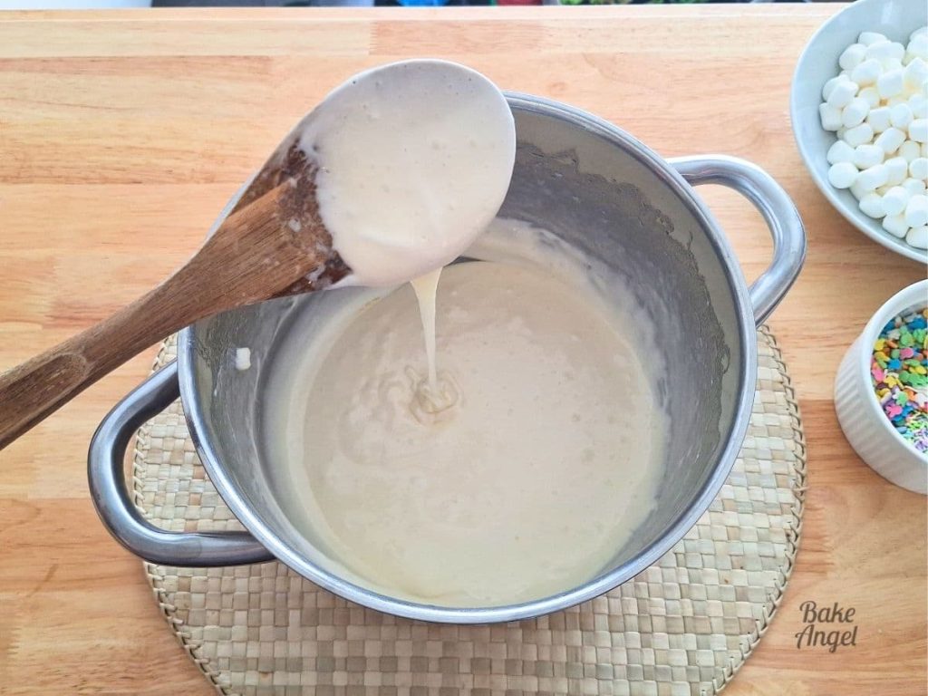 Melted butter and melted marshmallows in a large saucepan, with some dripping from a wooden spoon.