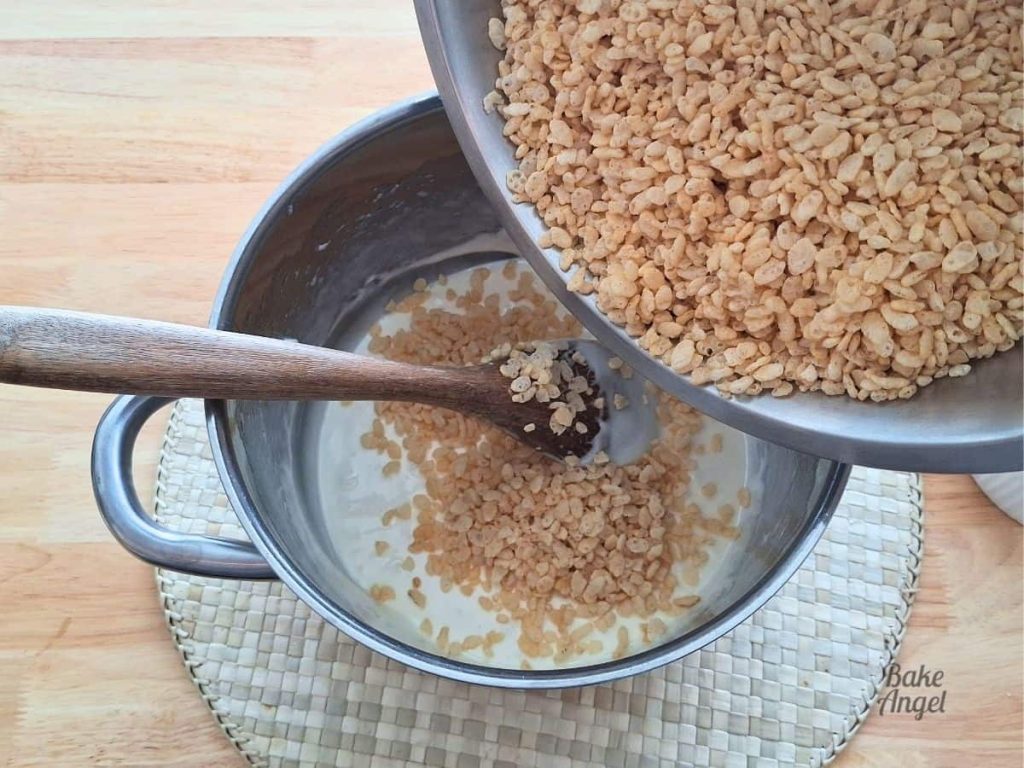 Rice cereal being added to a saucepan filled with melted butter and melted marshmallows.