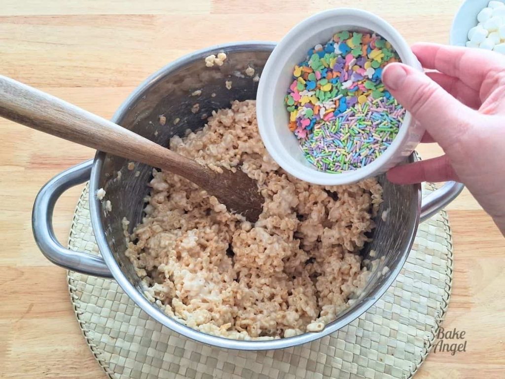 Adding Easter sprinkles to a saucepan filled with Rice Krispie Treats.