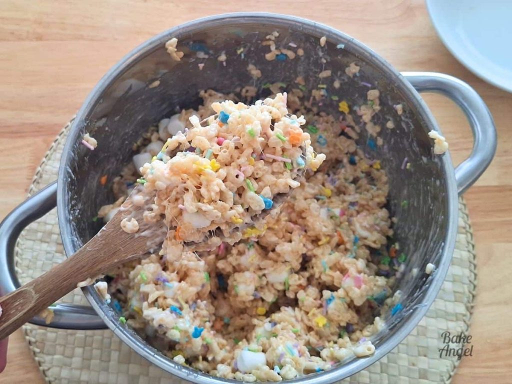 A spoonful of Easter Rice Krispie Treats on a wooden spoon, with the sprinkles being stirred in.