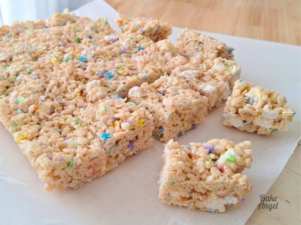 A side view of a slab of Easter Rice Krispie Treats on parchment paper with two small squares to the right.