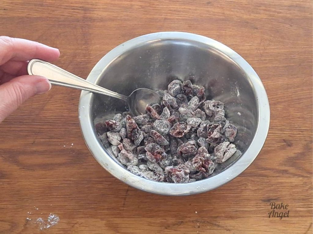 Dried cranberries being tossed in flour with a spoon.