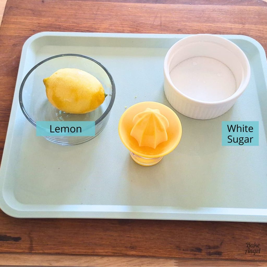 A lemon, a bowl of white sugar and a lemon zester on a light teal tray to make a lemon sugar glaze.