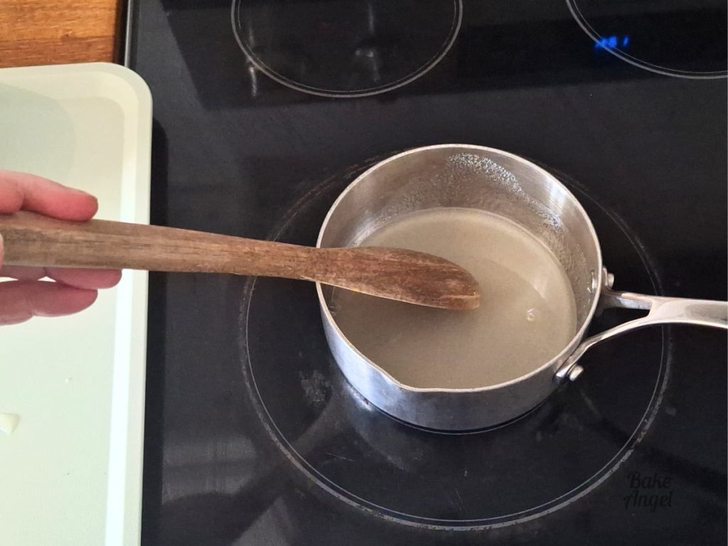 White sugar and lemon juice in a saucepan being stirred with a wooden spoon.