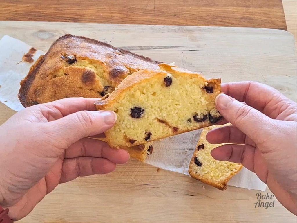 Close up of a slice of lemon cranberry loaf cake being held over a wooden cutting board.
