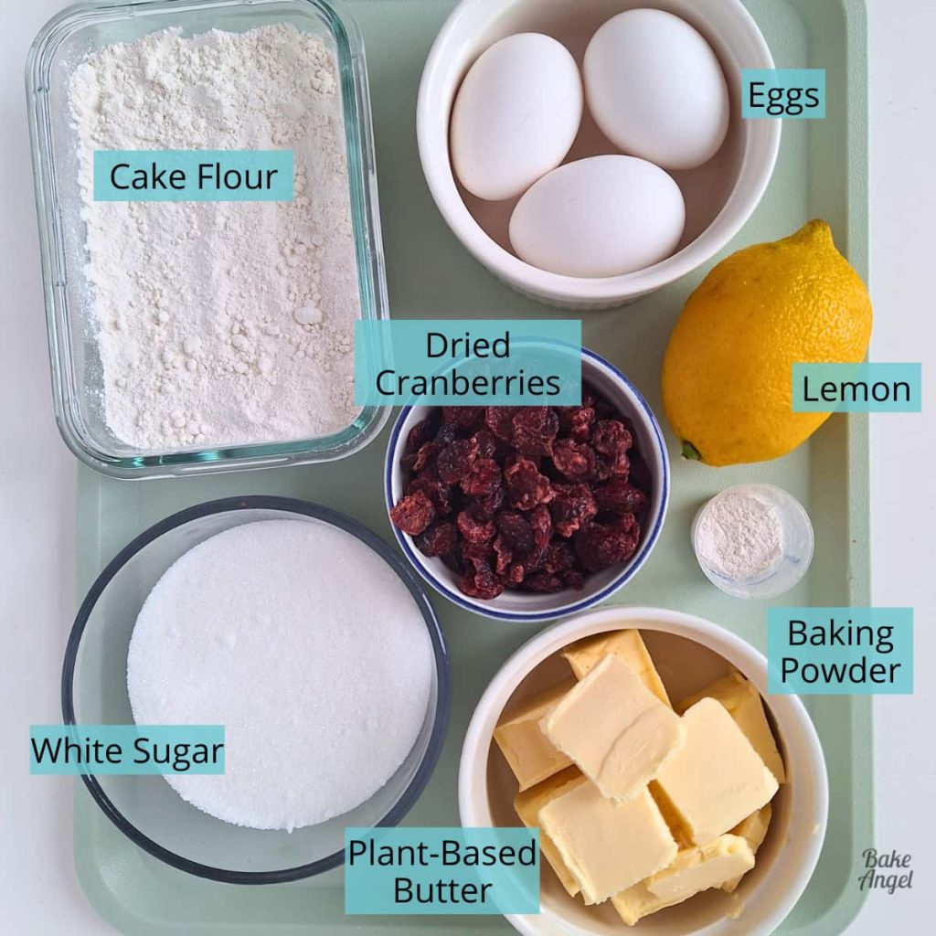 Ingredients measured out to make a dairy-free lemon cranberry cake: cake flour, 3 eggs, 1 lemon, dried cranberries, white sugar, butter, and baking powder.