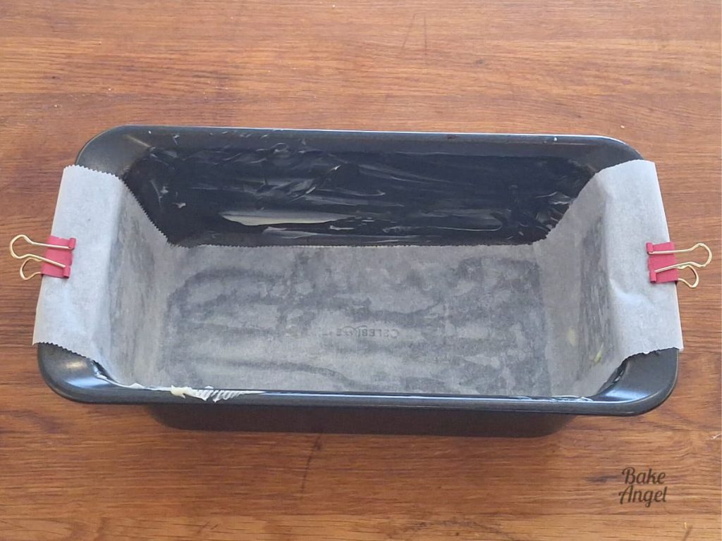 A loaf pan greased and lined with parchment paper. Two pink clips hold the edges of the paper in place.