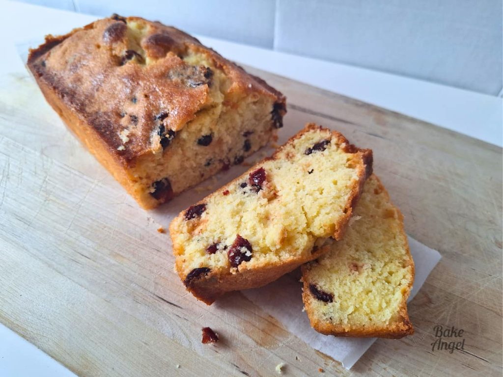 A wide shot of lemon cranberry loaf cake on a wooden board with two slices in the foreground and some crumbs on the board.