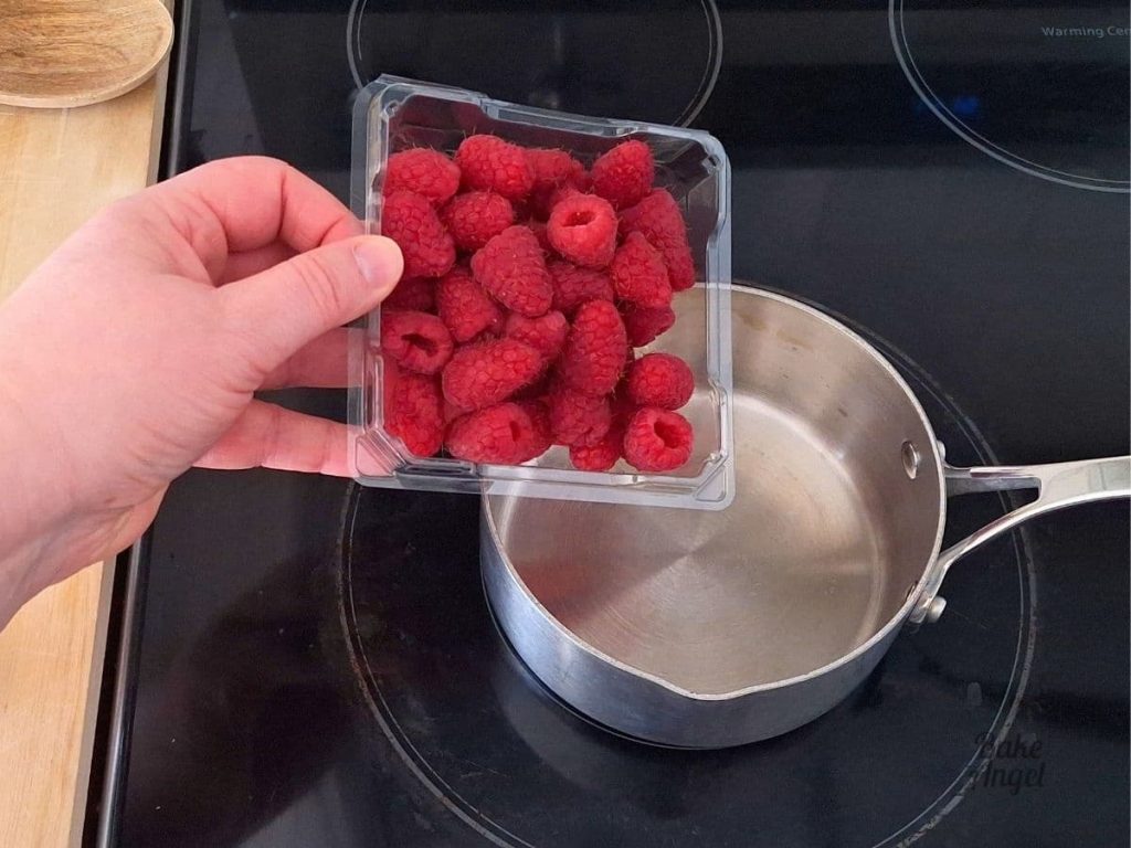 A small container of raspberries, held over a small saucepan on a stovetop.