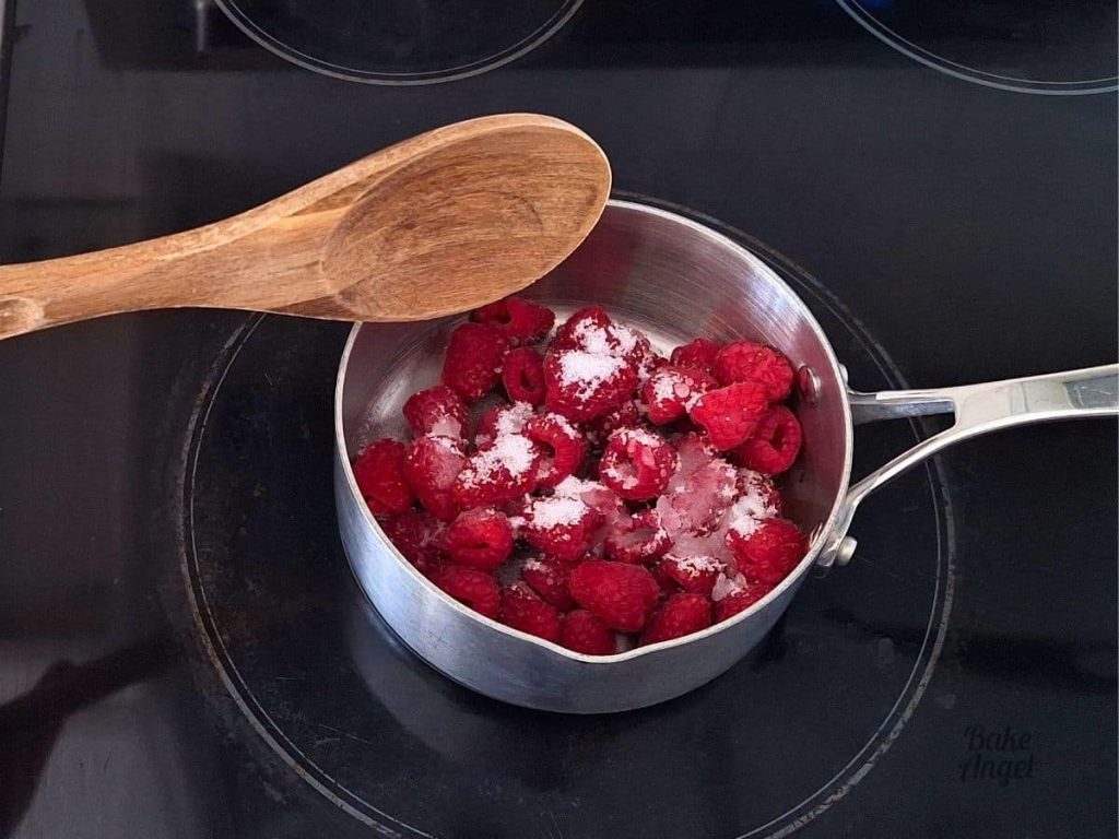 White sugar on top of raspberries in a small saucepan on a stovetop.