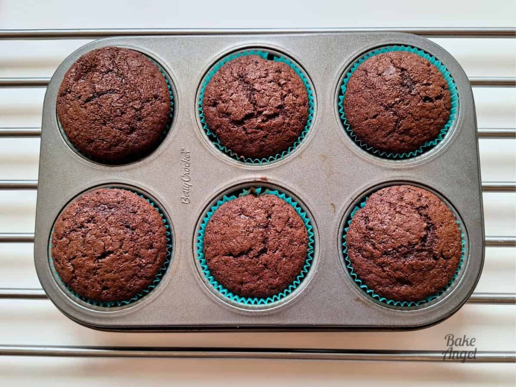 6 baked chocolate cupcakes in a baking pan on a cooling rack.
