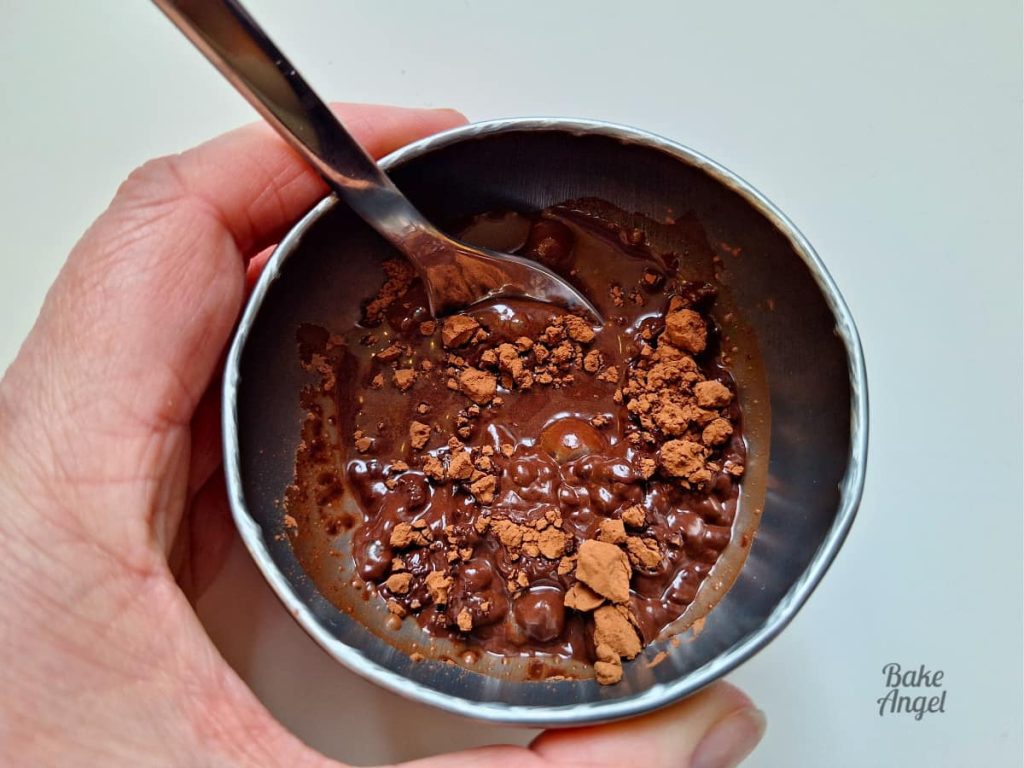 A small bowl with cocoa powder and water, being mixed with a spoon to form a paste.