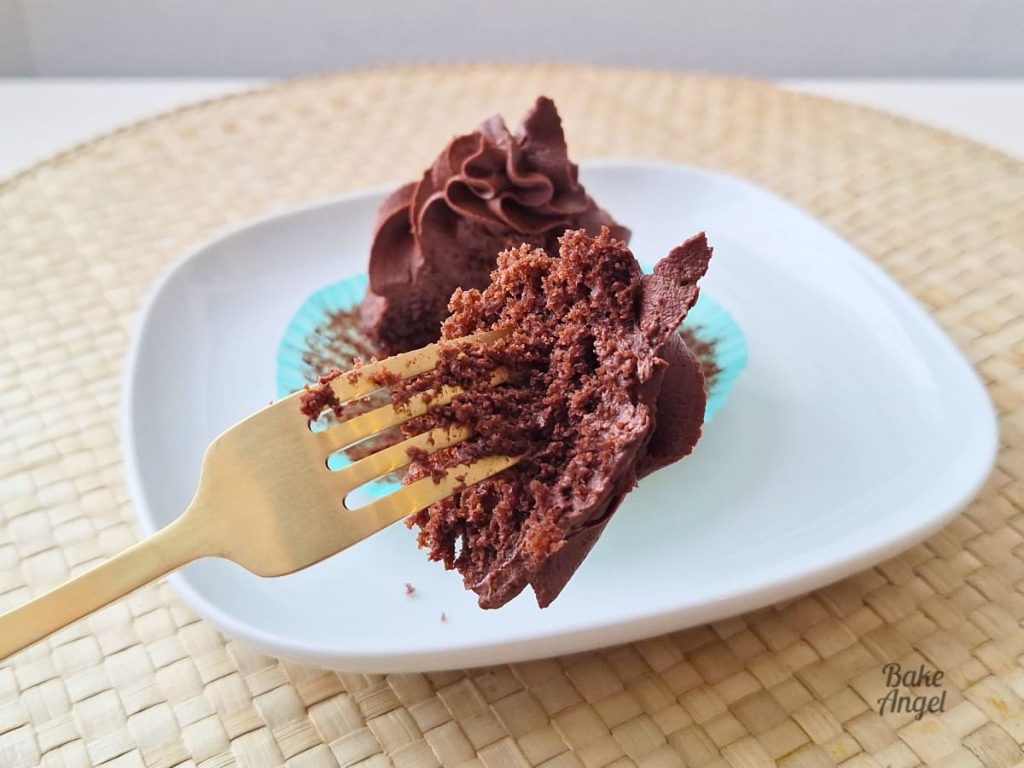 Close up of a piece of a chocolate cupcake on a gold fork, showing the crumb texture.