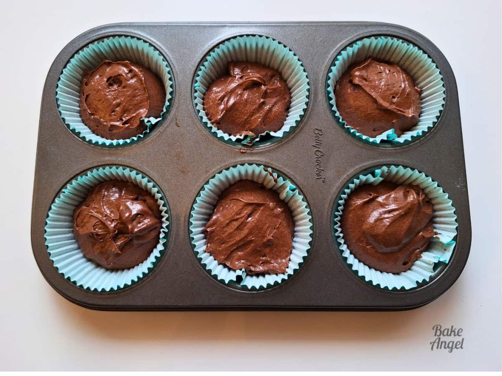 6 raw chocolate cupcakes in a baking pan before baking.