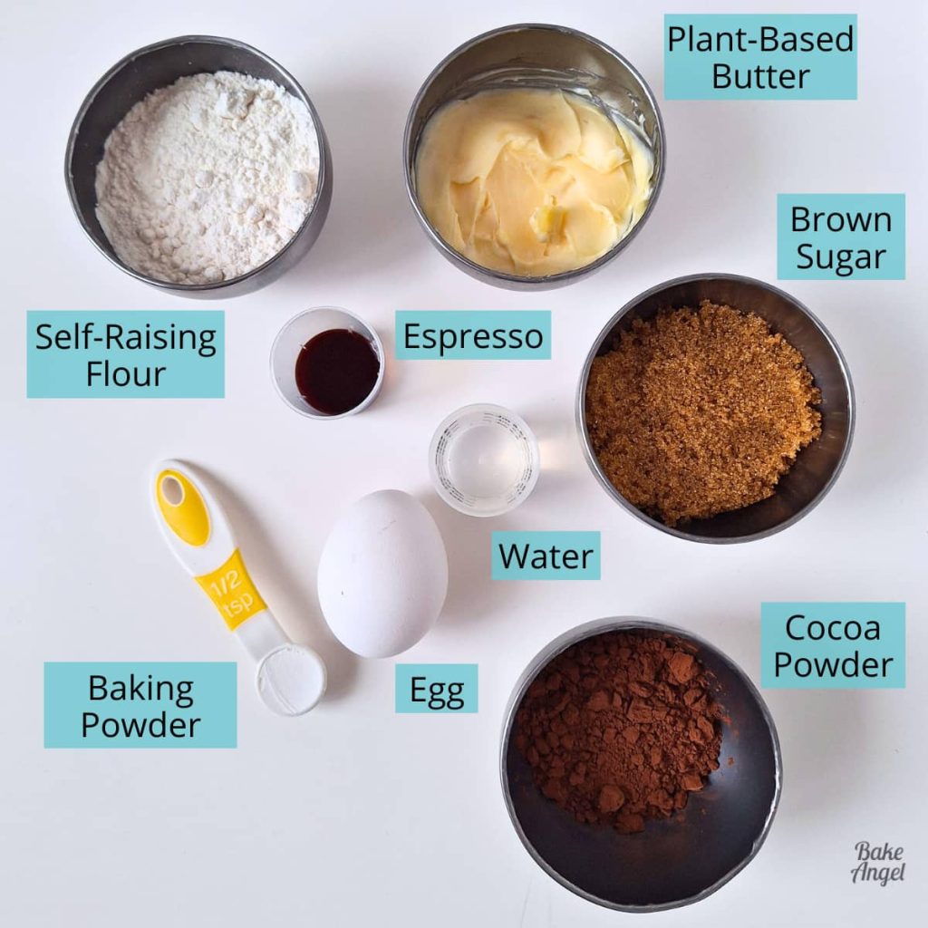 Ingredients measured out to make a small batch of chocolate cupcakes: self raising flour; plant based butter; espresso; brown sugar; water; one egg; baking powder; cocoa powder.
