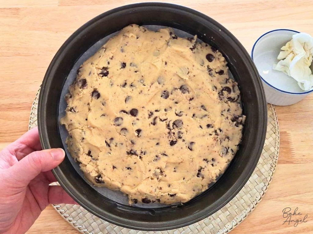 Raw chocolate chip cookie dough in a round cake pan with a generous gap around the outside to allow the cake to spread evenly when baking.
