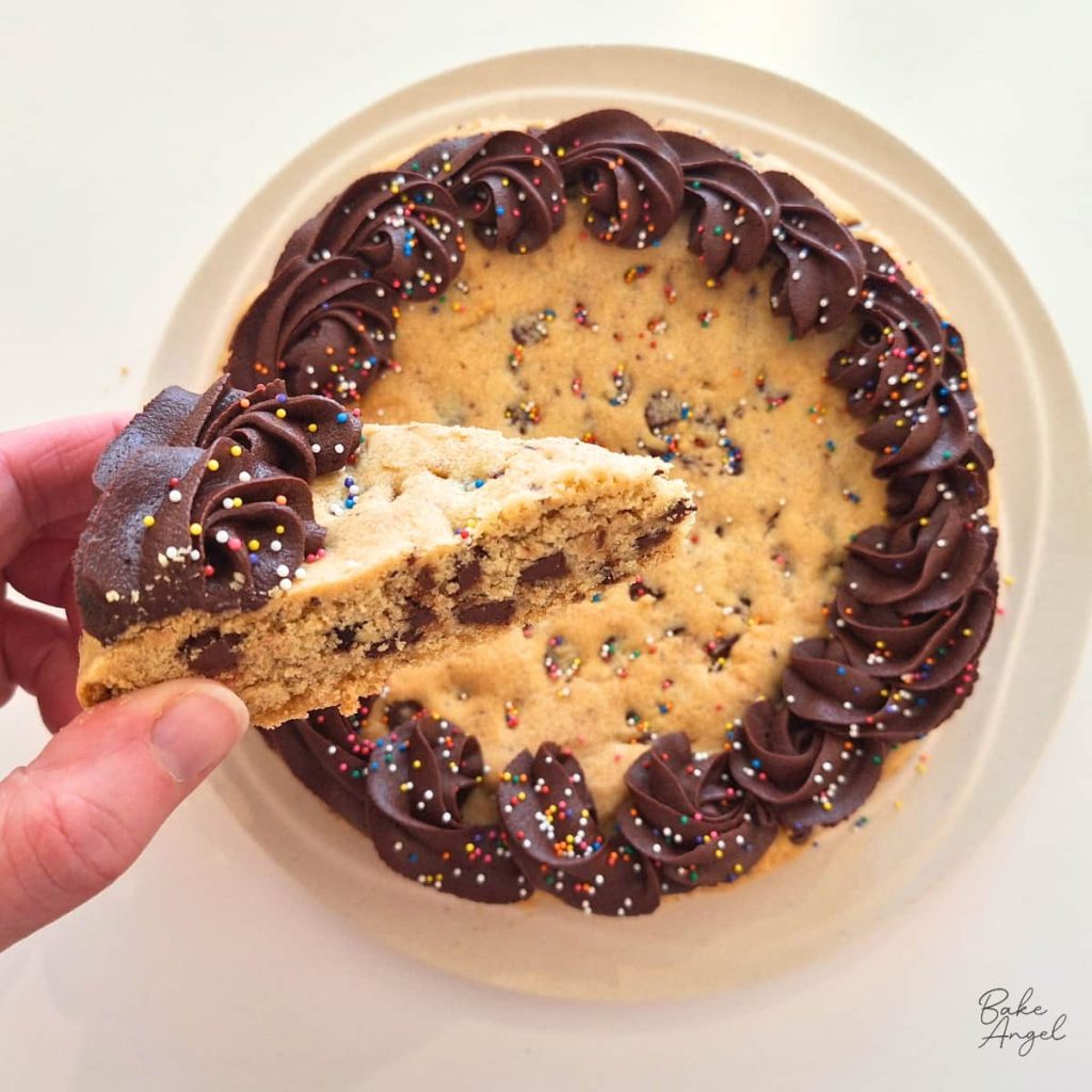 A slice of dairy free chocolate chip cookie cake with chocolate buttercream border being held