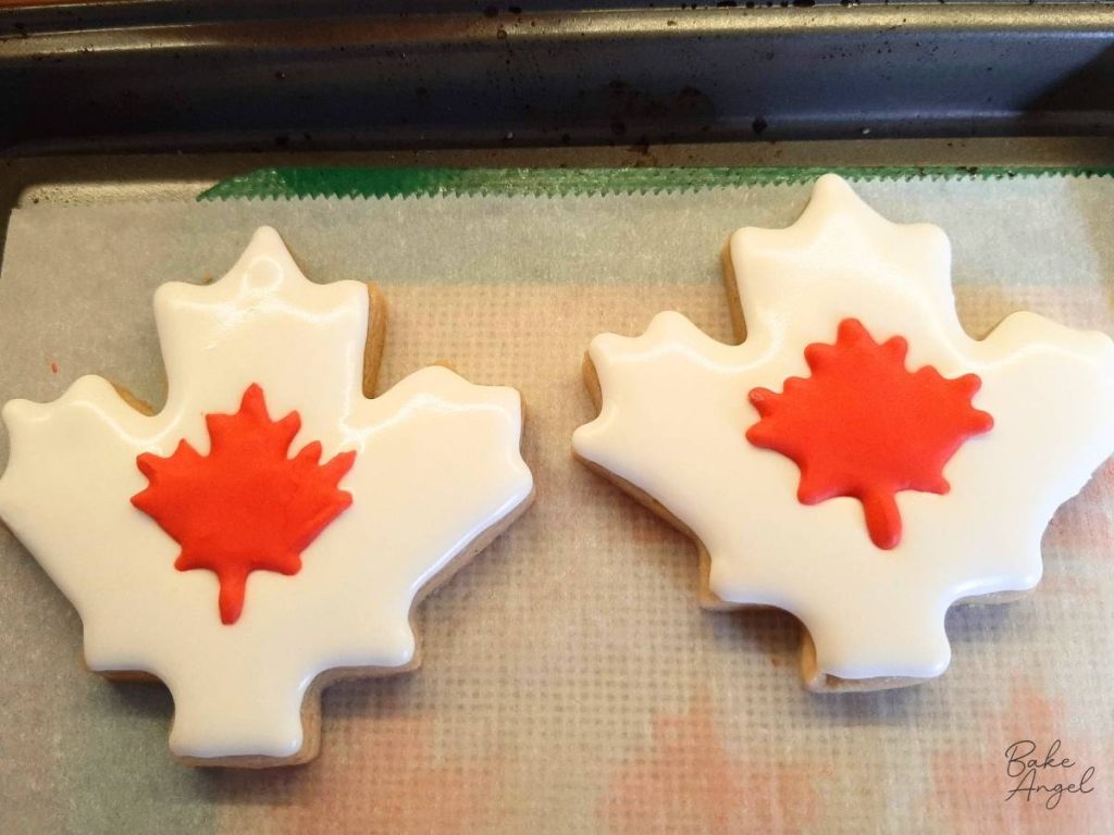 Two maple leaf sugar cookies drying on parchment paper.