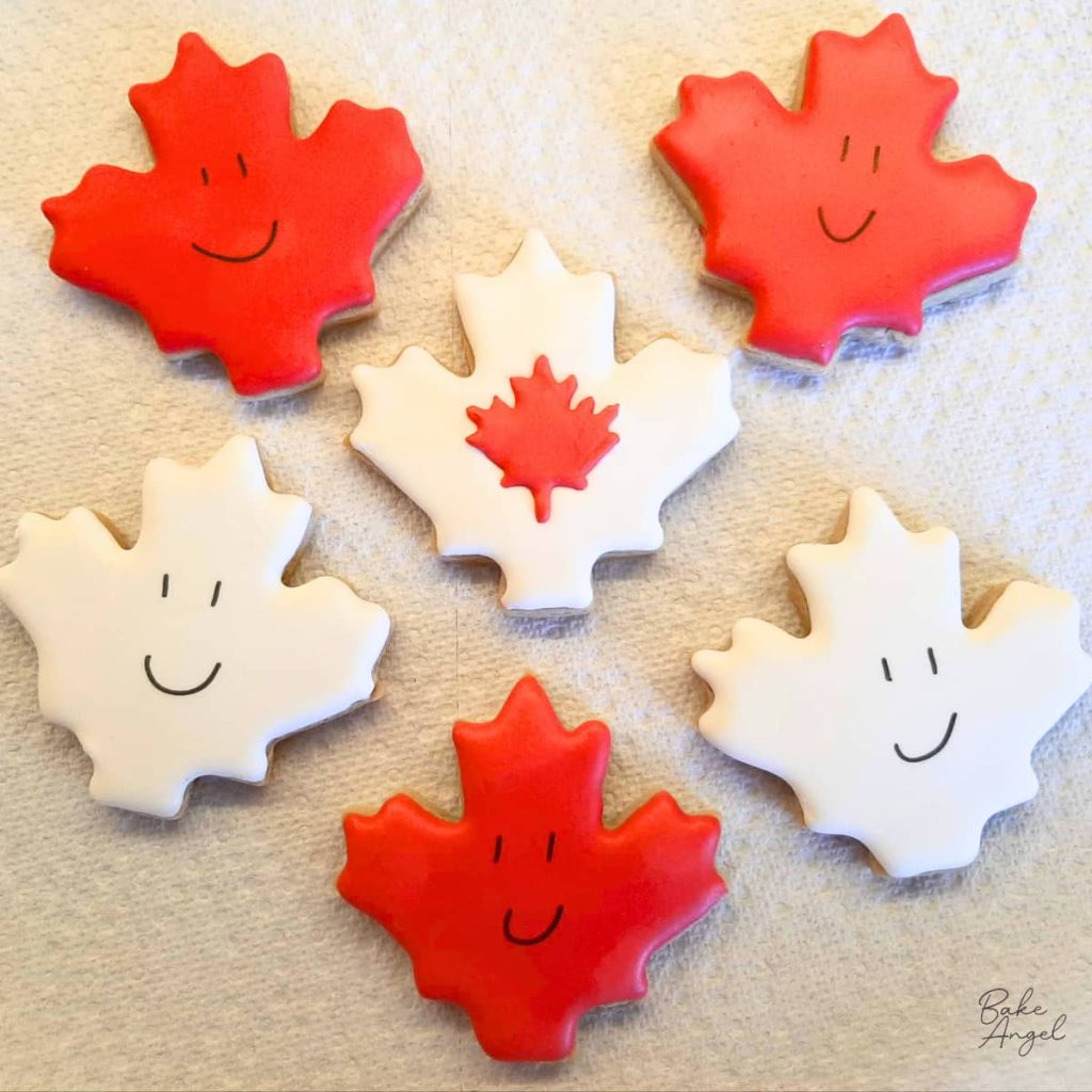 Decorated Canada Day sugar cookies with red and white maple leaf royal icing designs.