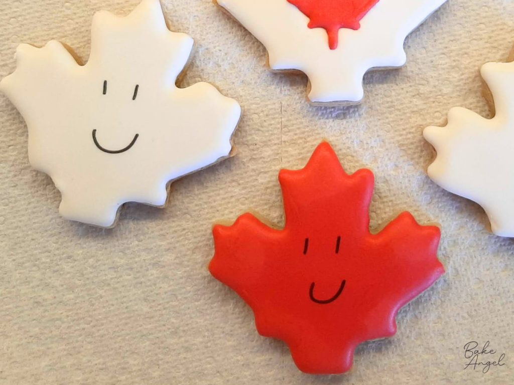 Canada Day sugar cookies decorated with a smiling maple leaf design.