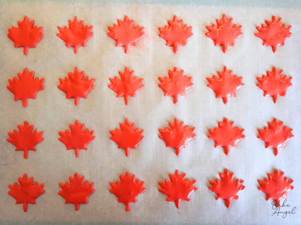 Finished maple leaf royal icing transfers drying on parchment paper.