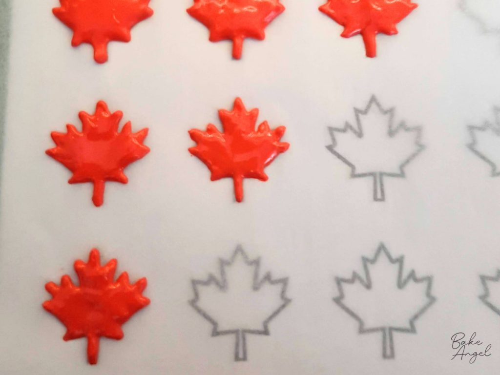 Red maple leaf royal icing transfers piped onto parchment paper.