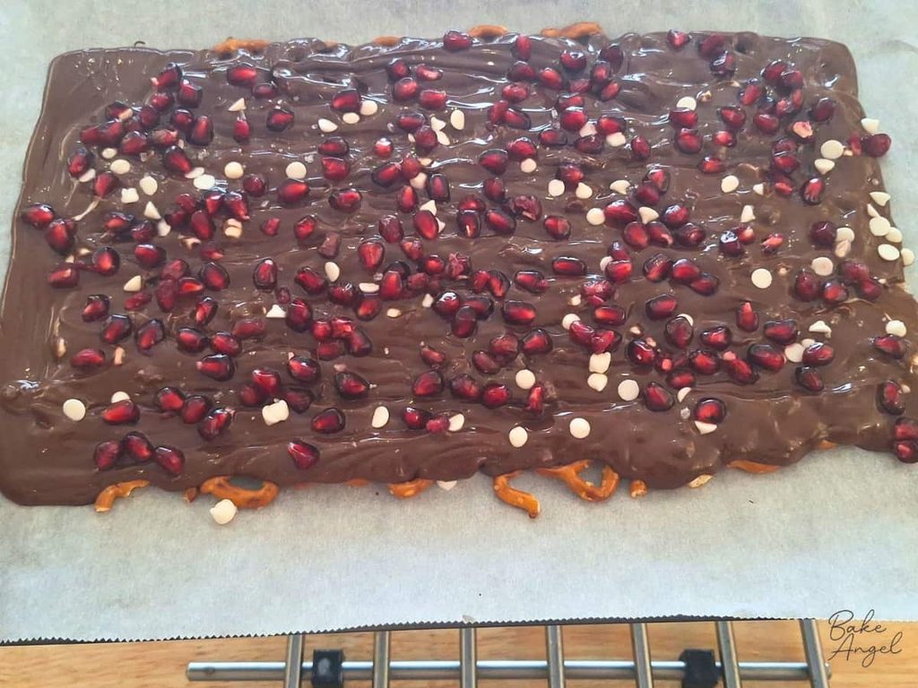 A tray of melted pretzel bark with pomegranate seeds and white chocolate chips on top.