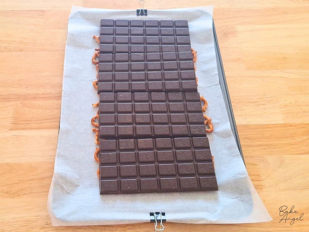 4 bars of dark chocolate on top of pretzels for making vegan pomegranate pretzel bark.