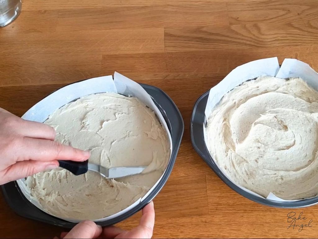 A spatula being used to spread cake batter into round baking pans.