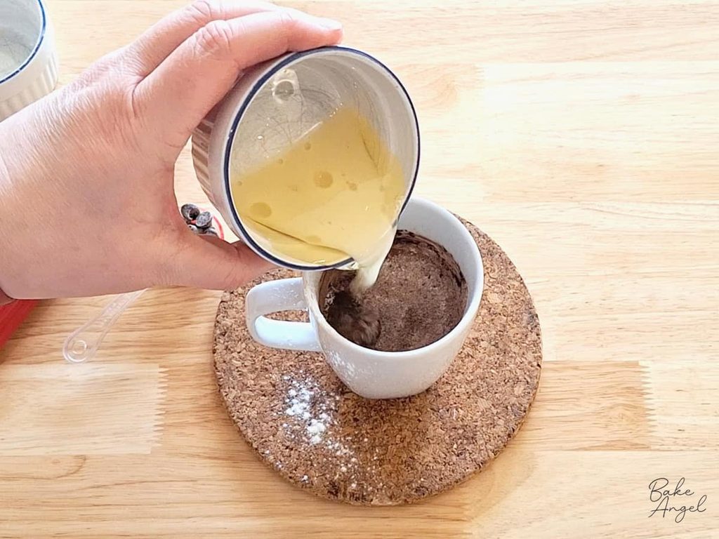 Oil and plant-based milk added to the dry ingredients in a mug to make chocolate cake batter.